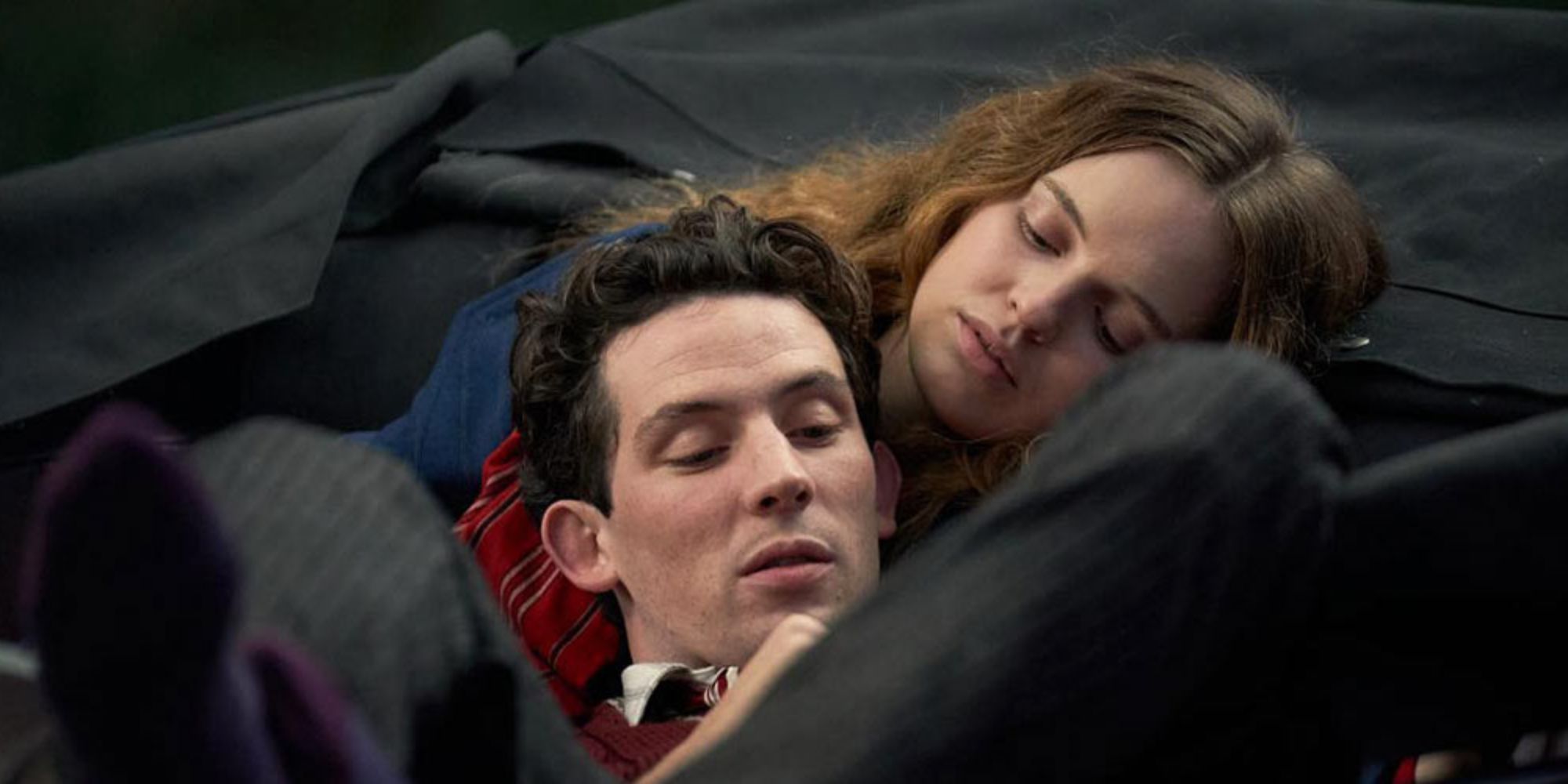 A man lays his head on a woman's chest as he reads