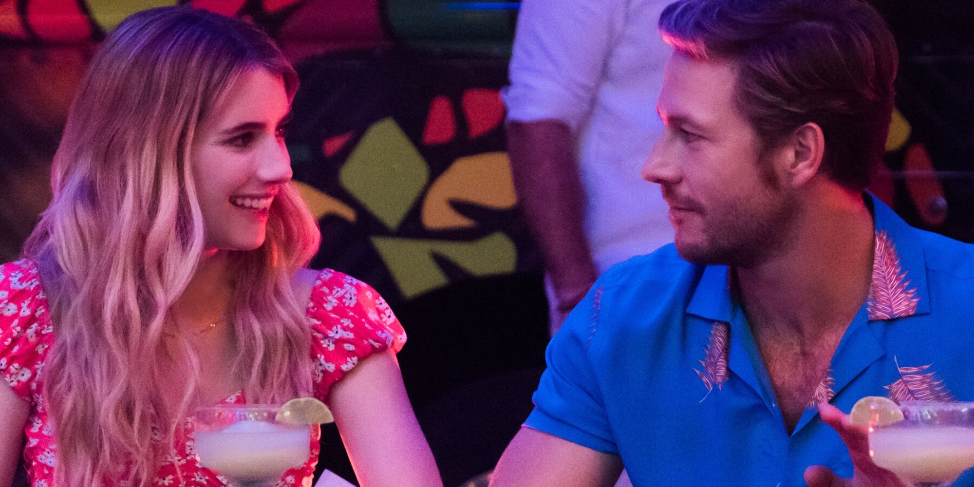 Emma Roberts and Luke Bracey as Sloane and Jackson looking at each other and smiling with margaritas in front of them in Holidate