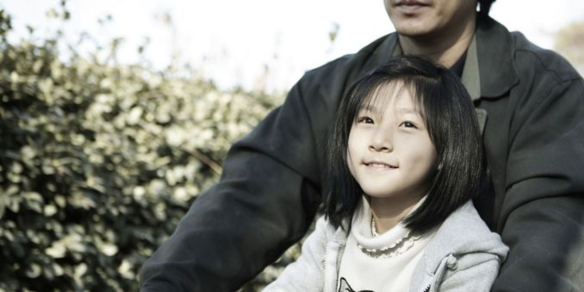 A child smiling as she rides on a bike with her father in A Brand New Life.