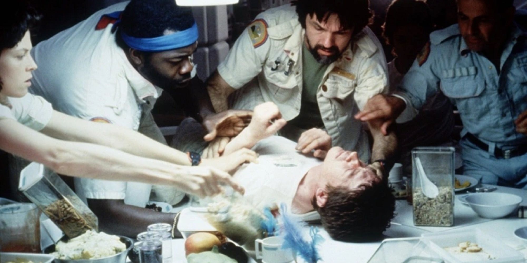 Several people gathered around a man lying on a table in the film Alien