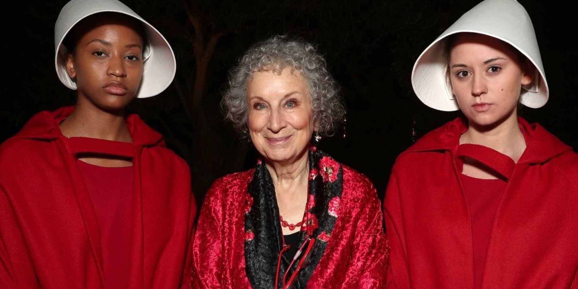 Margaret Atwood standing with two people dressed as handmaids