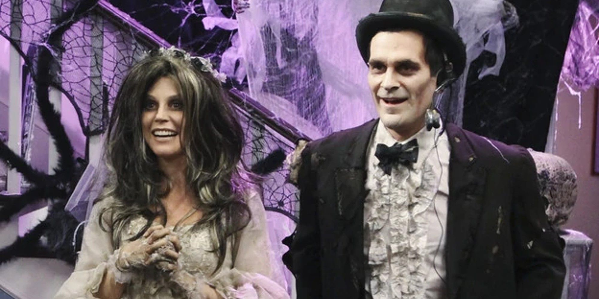 Claire and Phil stand next to each other dressed in undead bride and groom costumes and their house is lavishly decorated for Halloween in Modern Family.