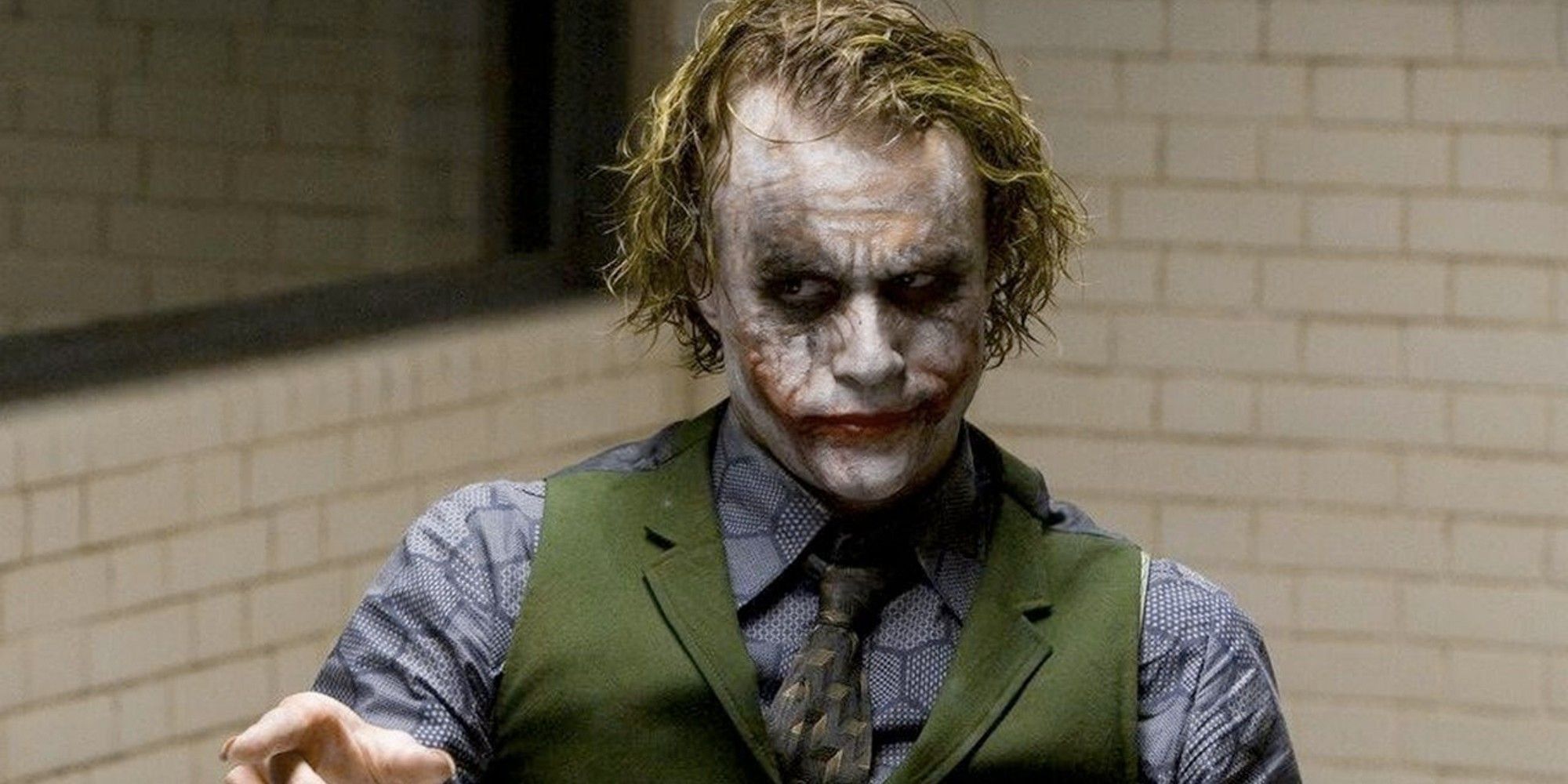 Joker sitting in an interrogation room pointing at someone off-camera in 'The Dark Knight'.