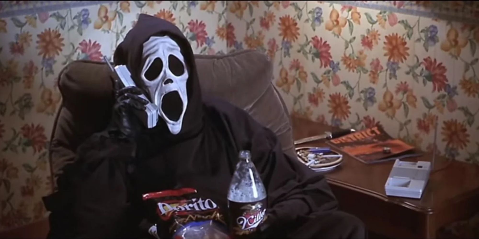 The masked killer from 'Scary Movie' sits on a sofa, talking on the phone with corn chips and soda in his lap.