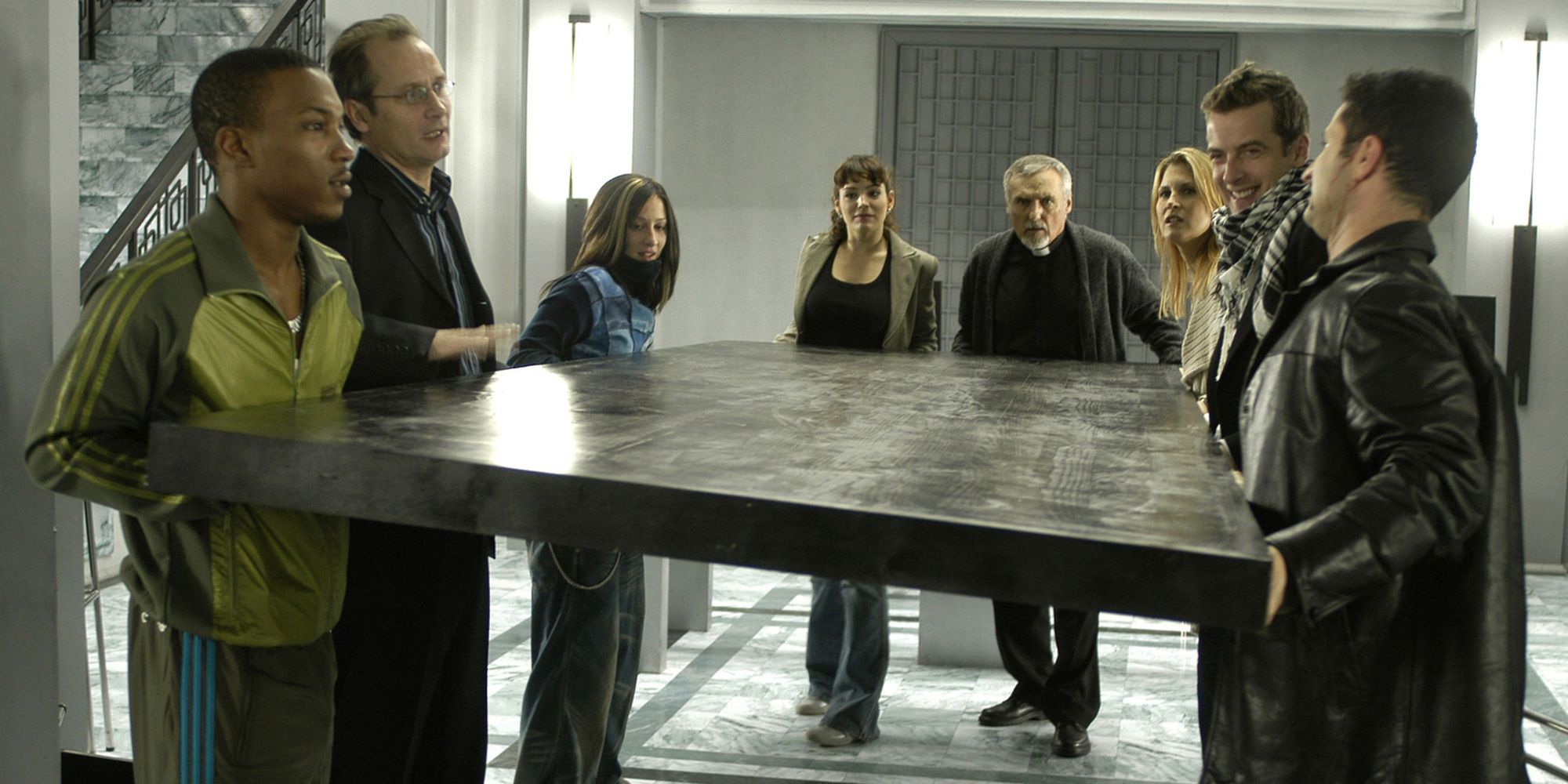 A group of people, including Dennis Hopper, Kelly Brook, and Peter Capaldi, carrying a table in House of 9