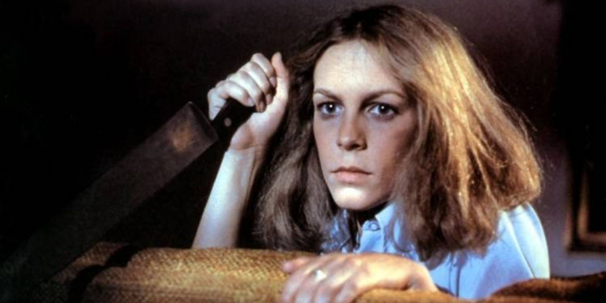 Jamie Lee Curtis peering over a couch with a butcher knife in Halloween