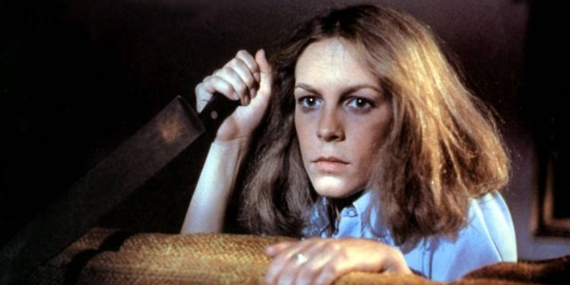 Jamie Lee Curtis regardant par-dessus un canapé avec un couteau de boucher dans Halloween.