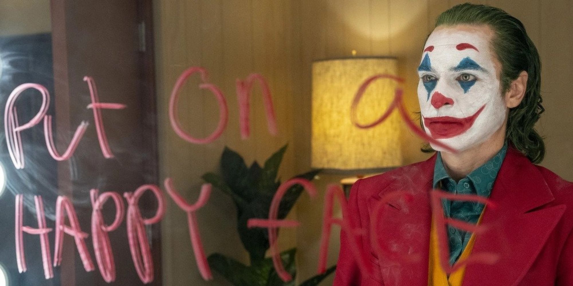 Joker standing in front of a mirror that says "put on a happy face"