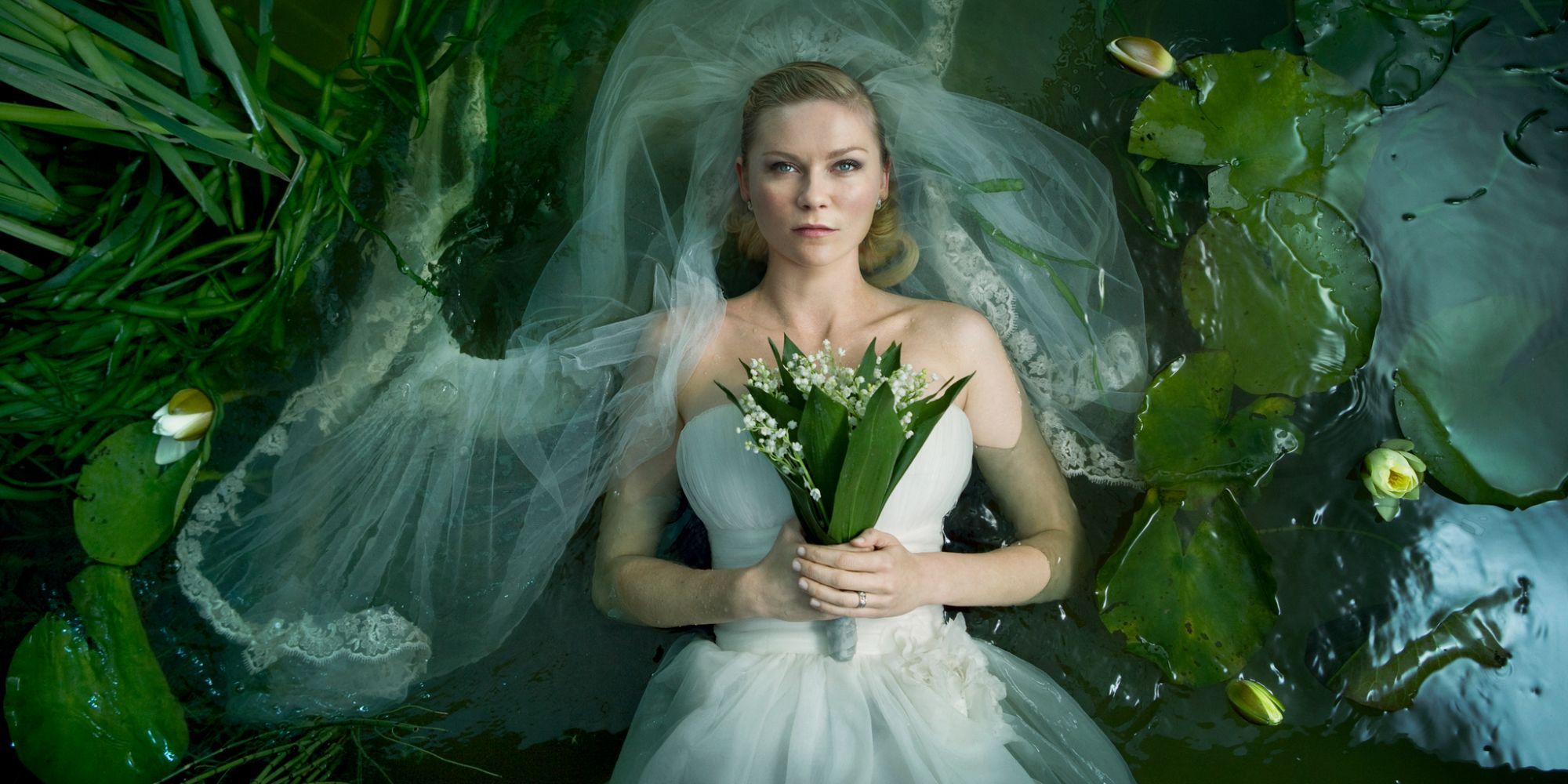 Kirsten Dunst on a wearing dress lying on a bed of water surrounded by leaves in a promo image for Melancholia.