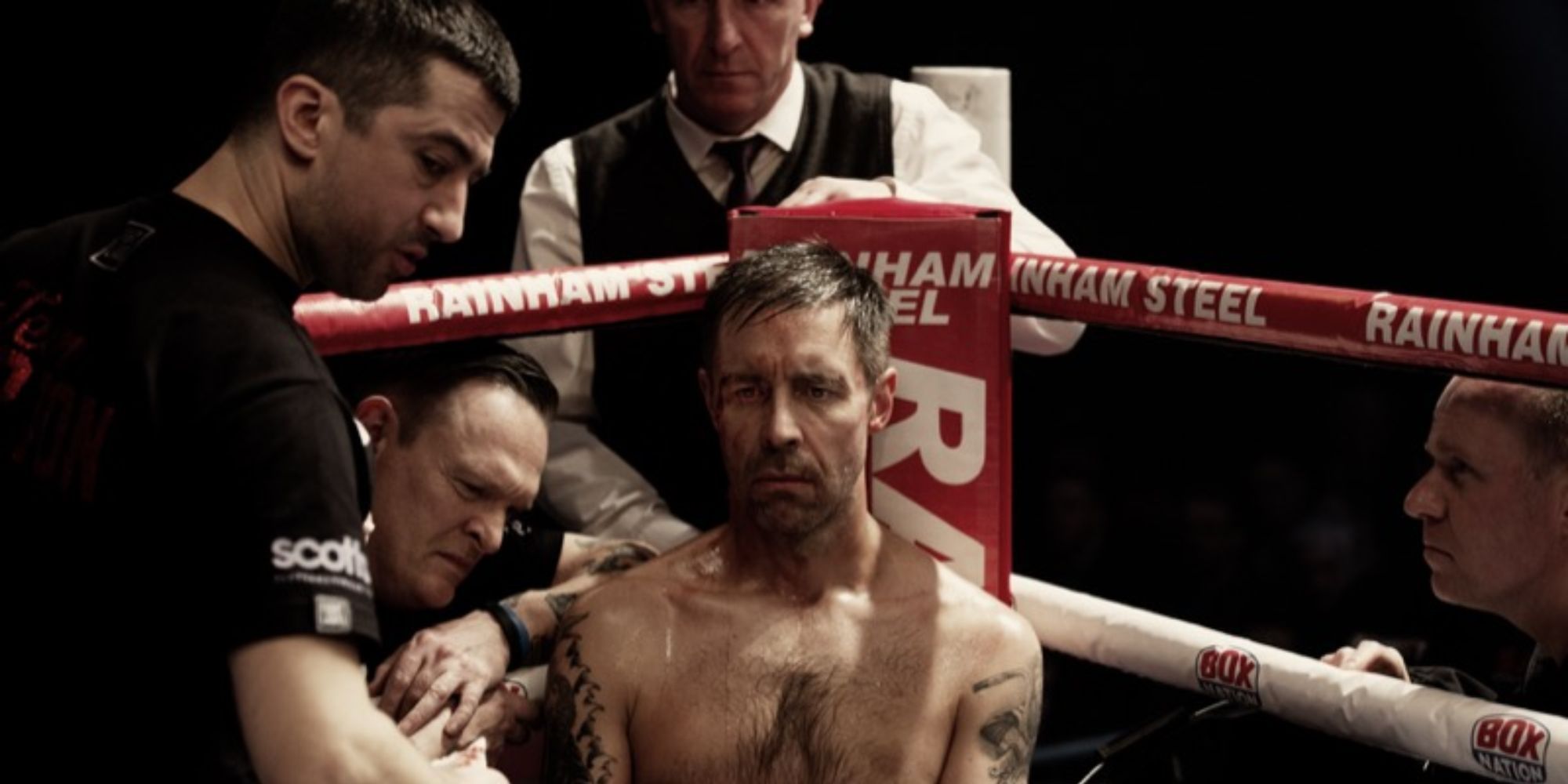 A man sitting broody at the ring corner with people surrounding him