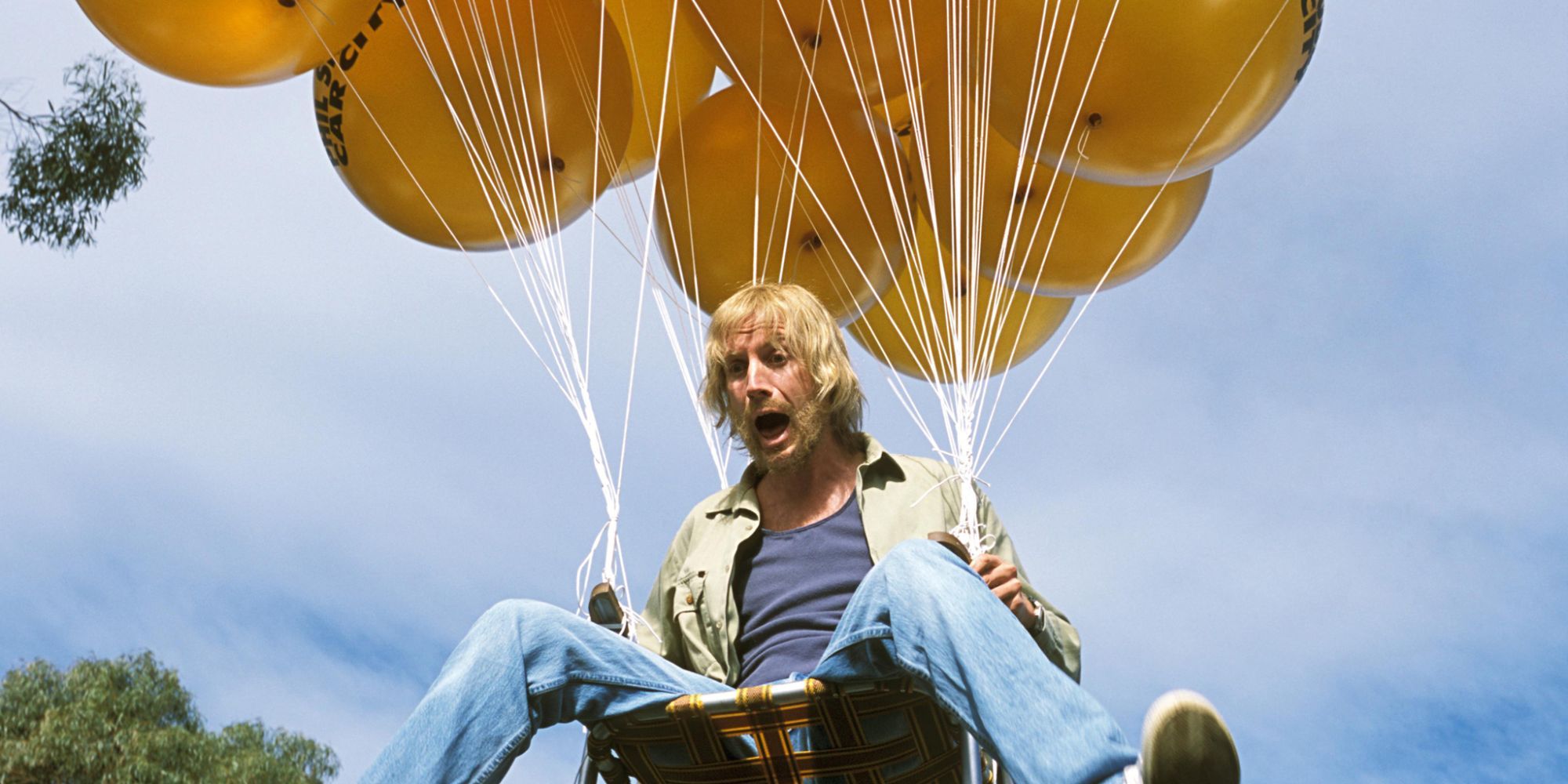 A man sitting on a chair that attached to baloons