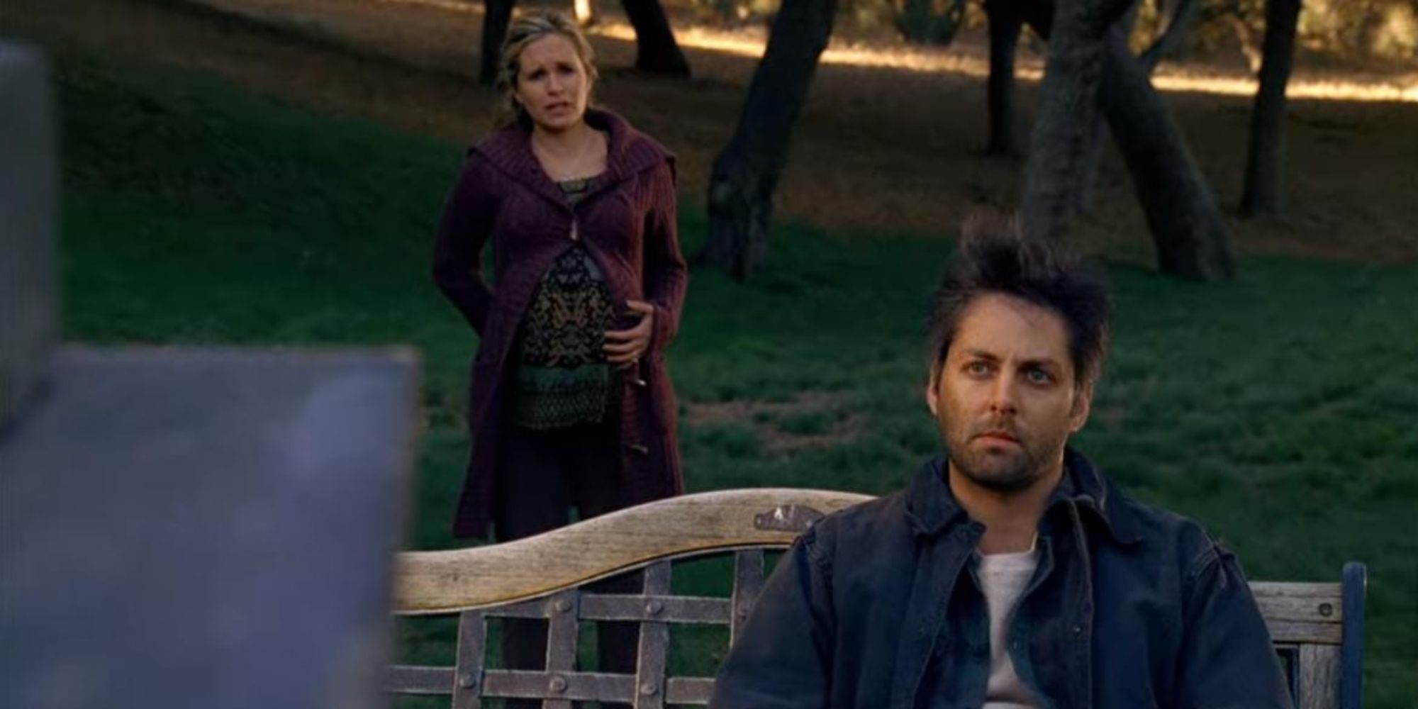 a man sitting on the bench with a pregnant woman walking towards from behind