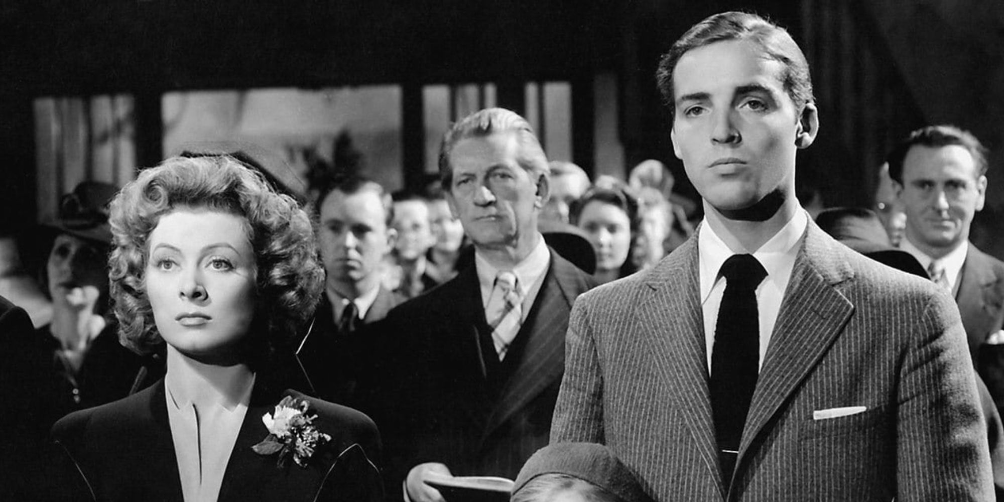 Kay and Toby Miniver standing in a crowd looking firmly ahead in Mrs. Miniver - 1942