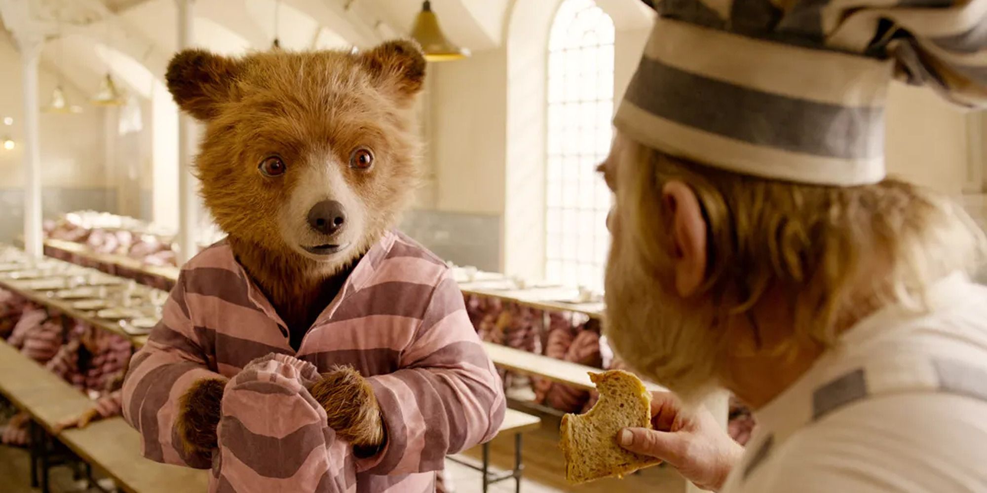 Paddington con uniforme rosa de prisión hablando con sus compañeros de prisión en 'Paddington 2'