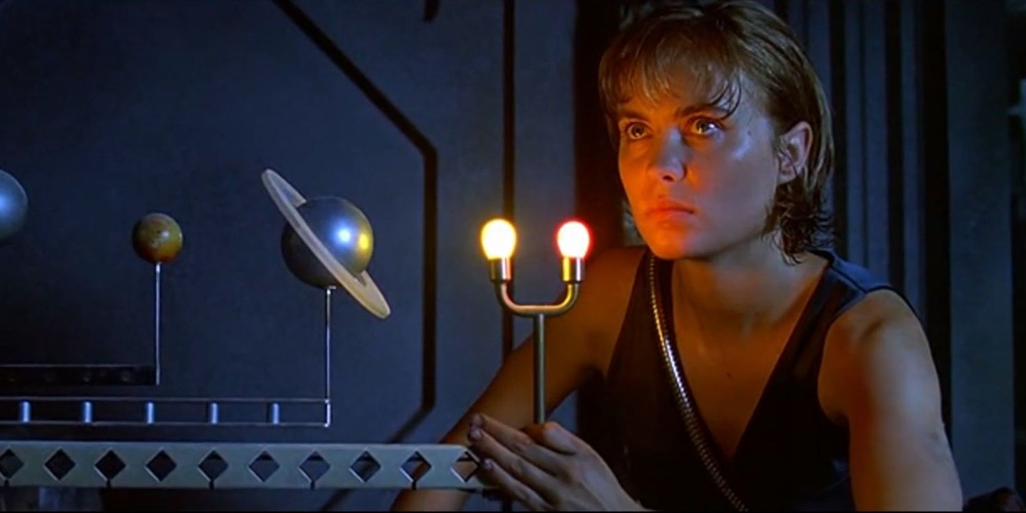 A woman kneels down next to a machine with planet figurines and two lights coming from it in Pitch Black.