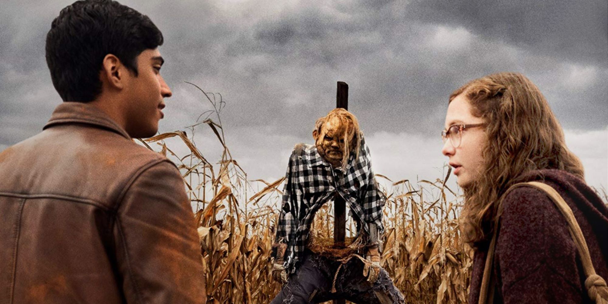 A young man and woman stand in a corn field with a menacing scarecrow behind them