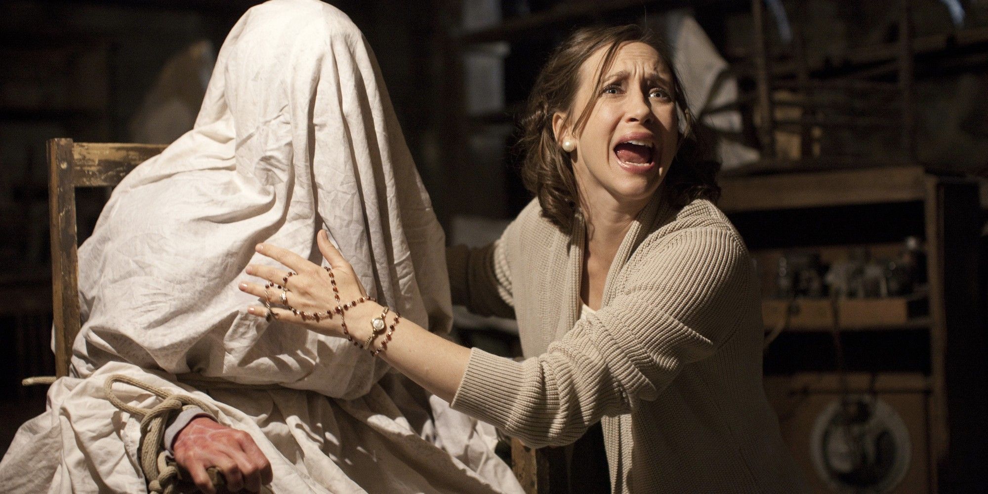 Vera Farmiga as Lorraine Warren, crying out next to a woman bound and covered in a sheet in The Conjuring