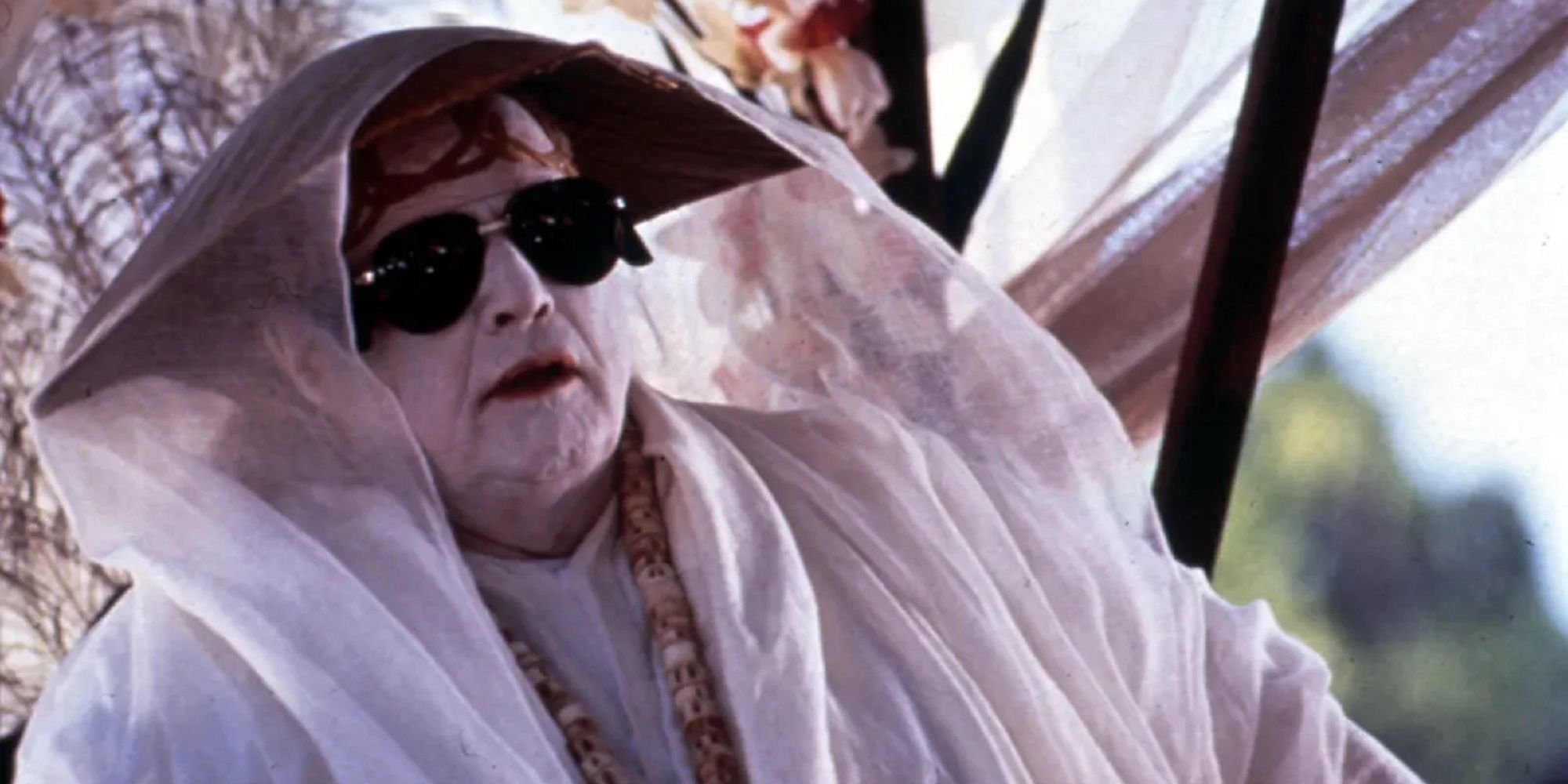 Marlon Brando as Dr. Moreau sitting under a small tent wearing a hate and white covering in The Island of Dr. Moreau