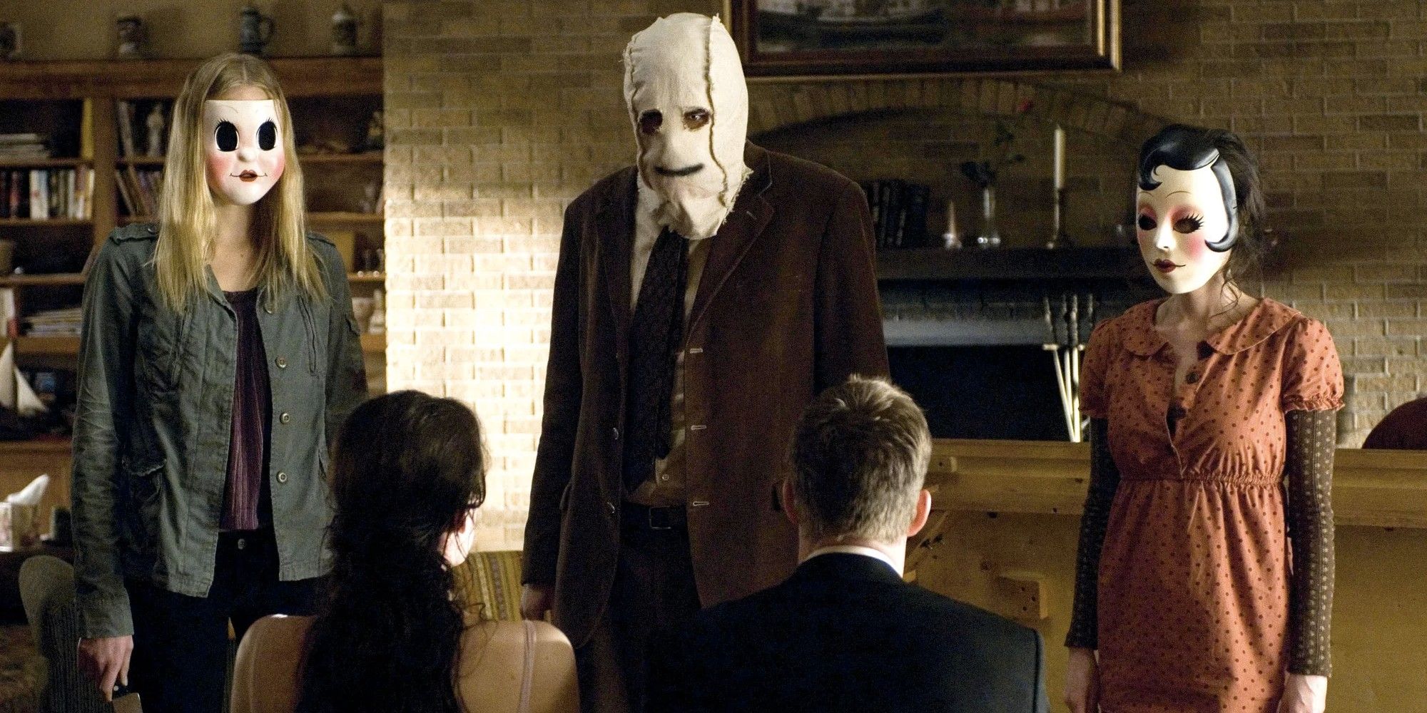 Three masked figures looking down at a couple tied down in chairs in the 2008 movie 'The Strangers'