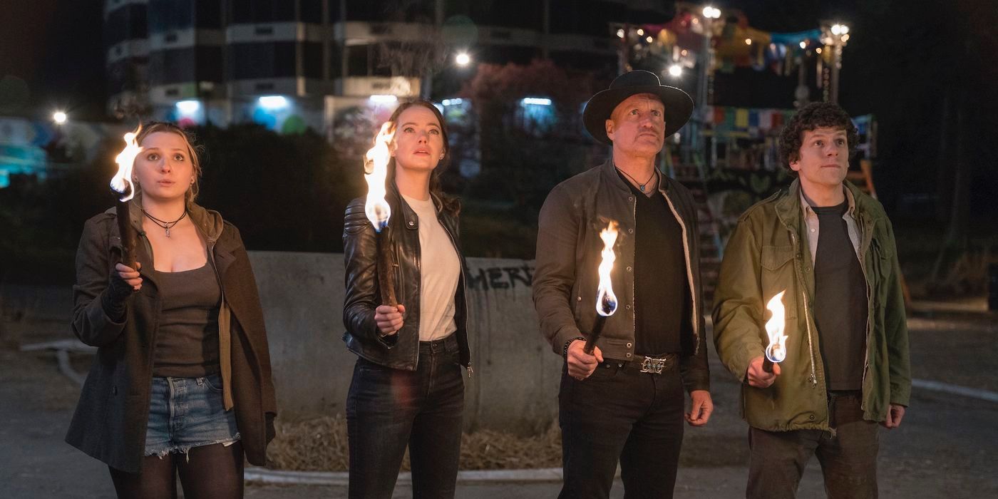 The cast hold flaming torches and look up while standing outside at night in Zombieland: Double Tap.