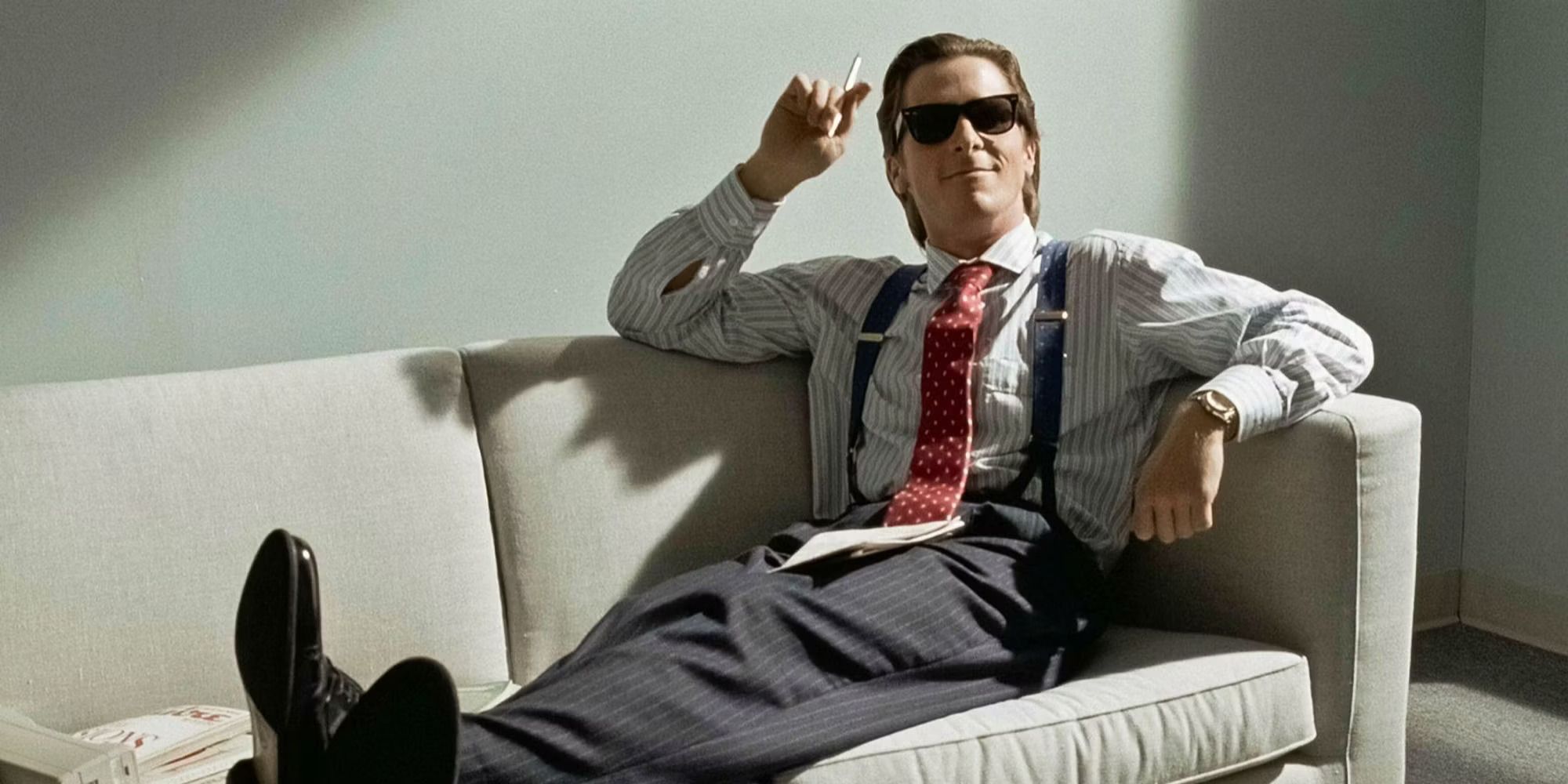 Patrick Bateman on a couch smoking and wearing sunglasses in 'American Psycho'