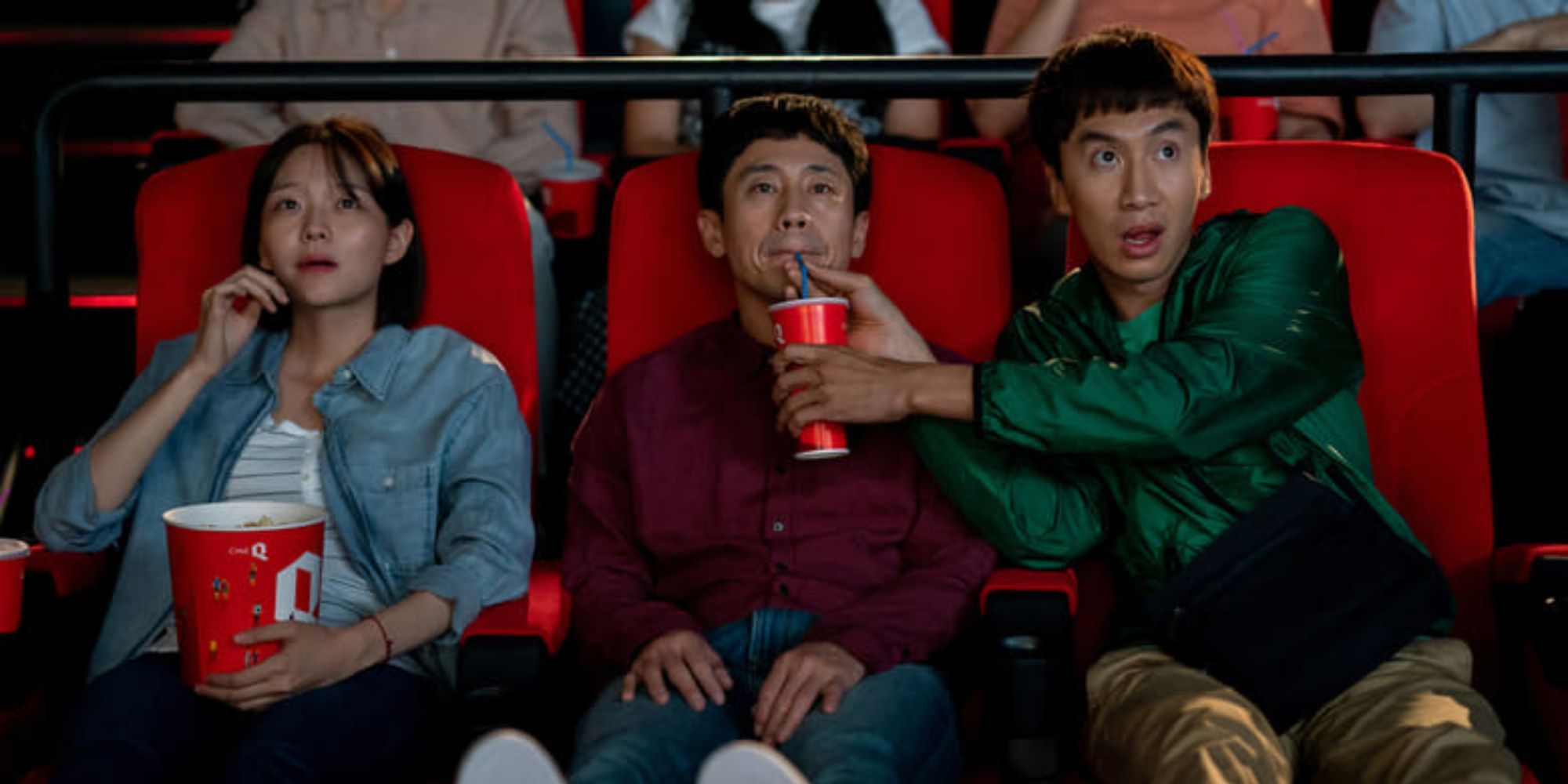 Three people watch a movie in a theater as one man holds a drink up so the other can drink in Inseparable Bros.
