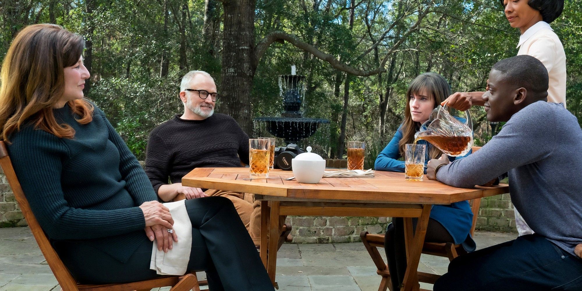 Une famille assise sur la table pendant qu'une femme noire leur verse du thé dans Get Out.