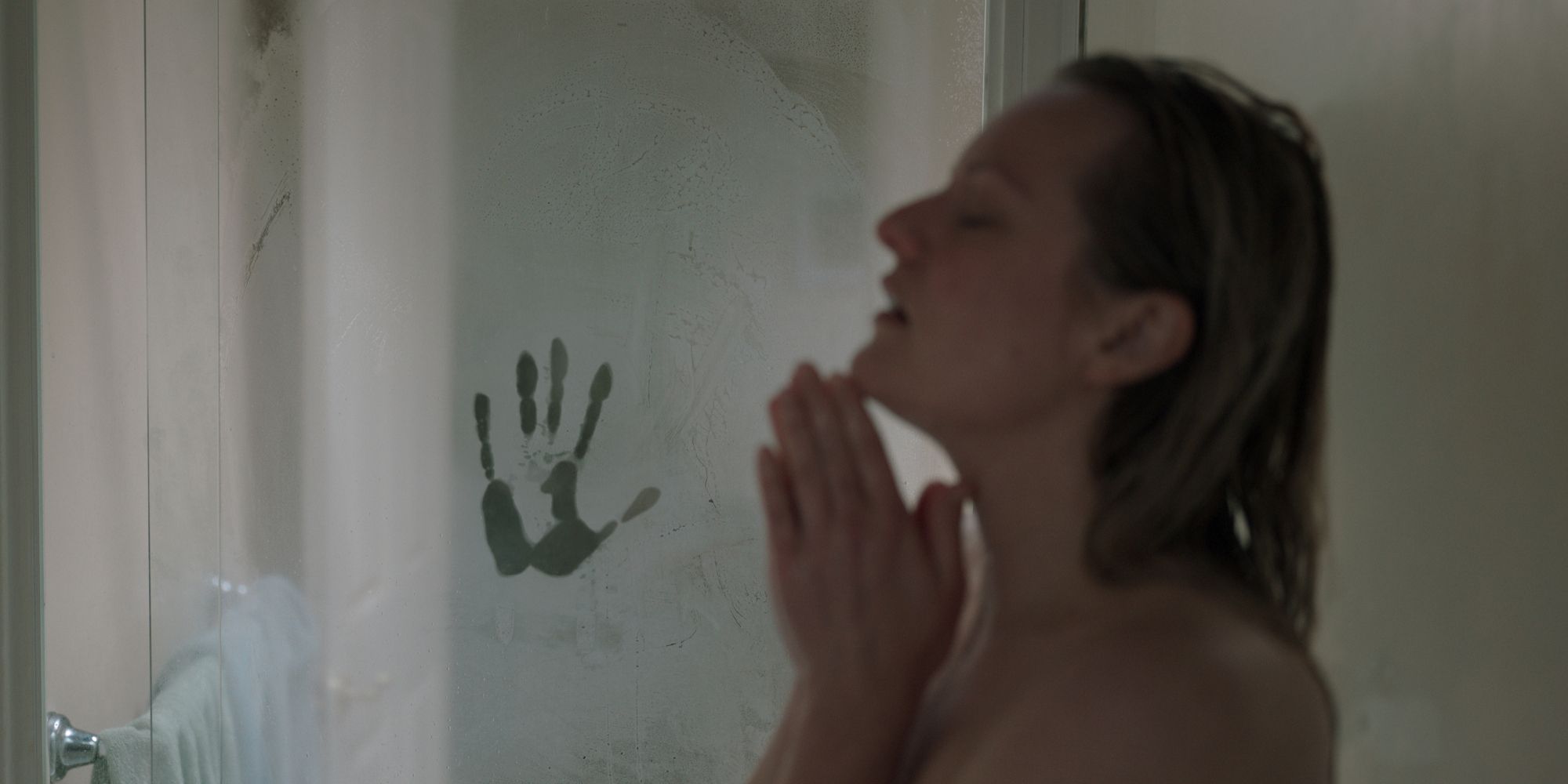 Cecilia showering while a human handprint appear on the glass in The Invisible Man