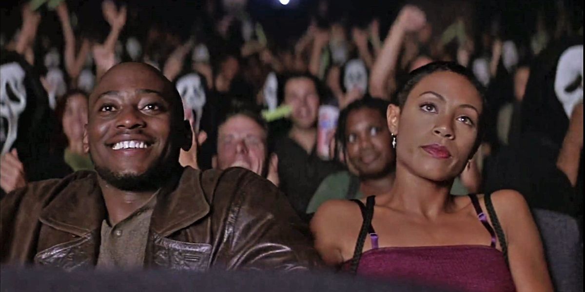 Omar Epps et Jada Pinkett Smith assis dans une salle de cinéma entourés de Ghostfaces dans Scream 2.
