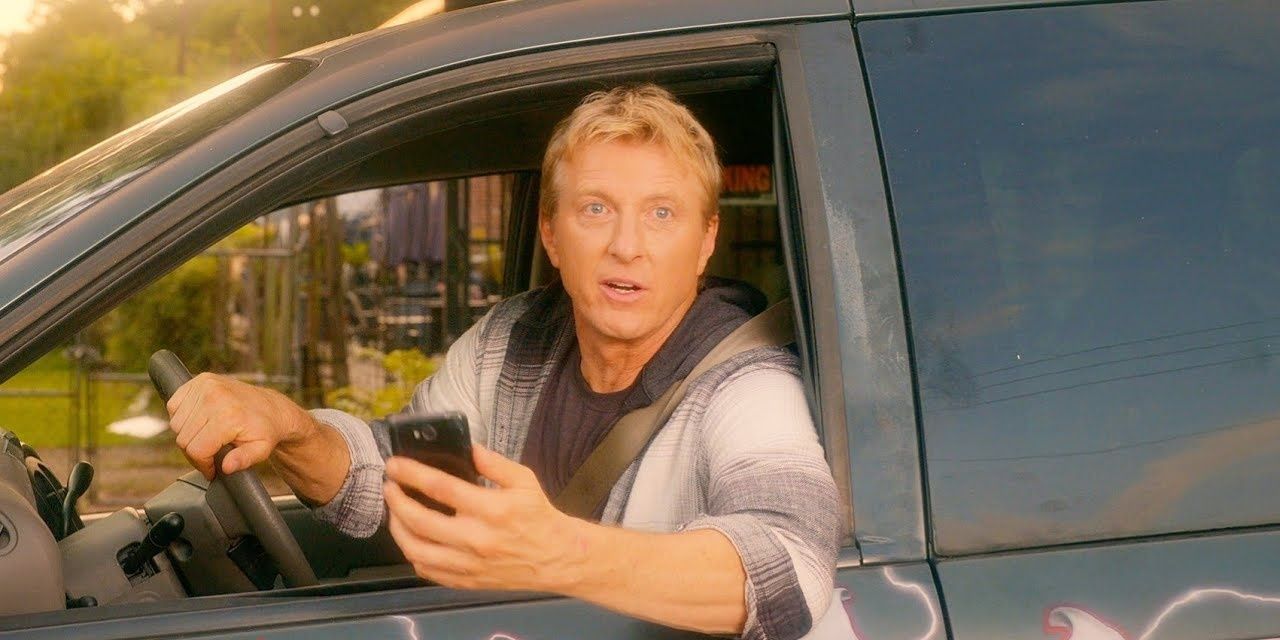 Johnny on Cobra Kai sitting in the driver's seat of a car, holding his phone and talking out the window.