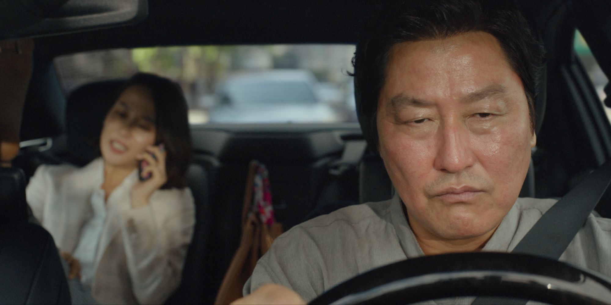 Song Kang-ho as Kim Ki-taek, looking annoyed while driving Cho Yeo-jeong as Choi Yeon-gyo, who sits in the back of the car, in Parasite