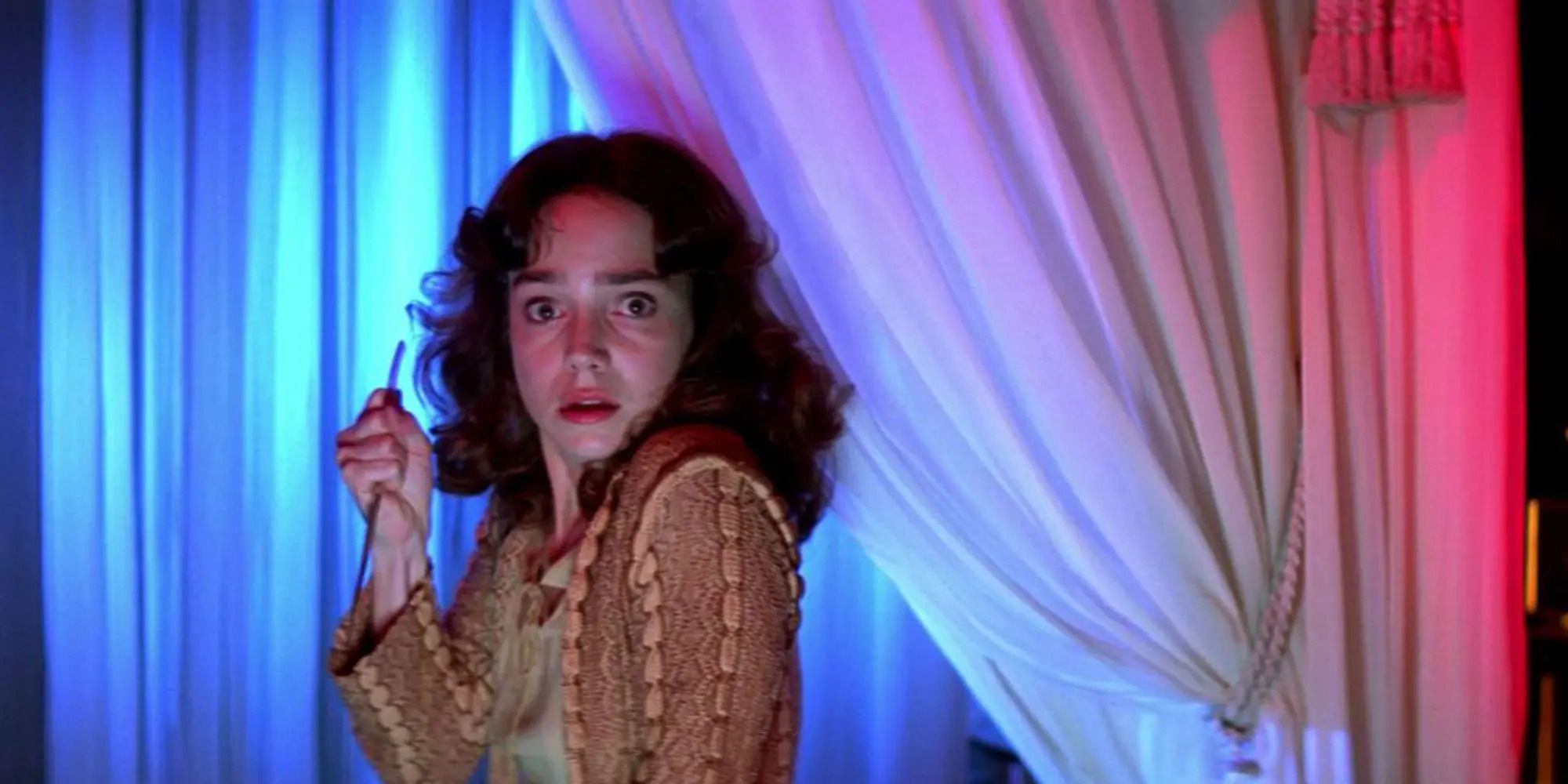 Suzy (Jessica Harper) holding a knife while standing in front of curtains in 'Suspiria'