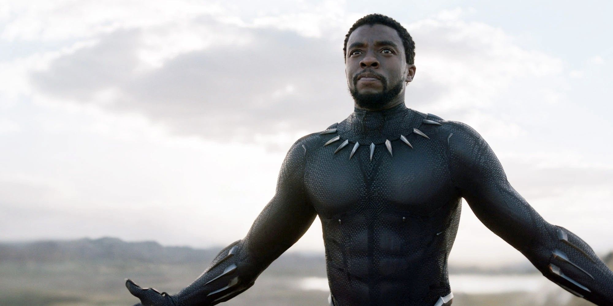 Chadwick Boseman, quien interpreta a T'Challa, también conocido como Black Panther, se quita la máscara y abre los brazos.