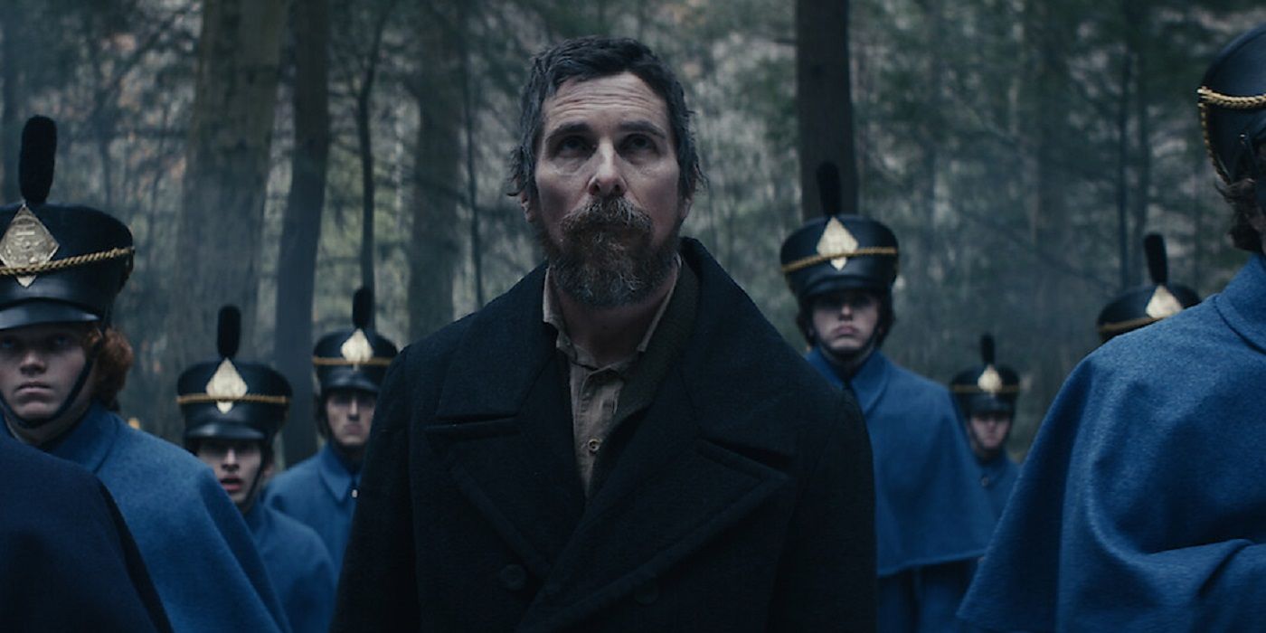 Christian Bale como Landor olhando para algo com cadetes ao seu redor na floresta em The Pale Blue Eye