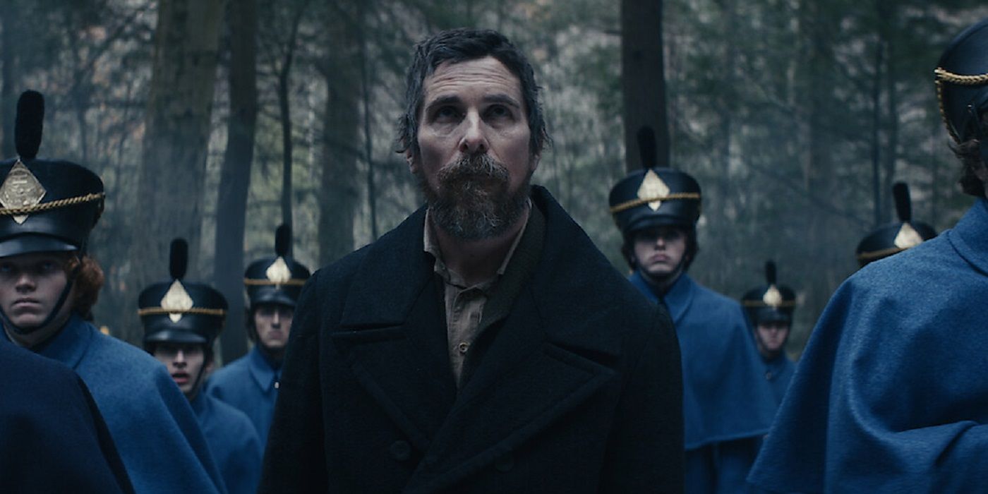 Christian Bale as Landor looking up at something with cadets around him in the woods in The Pale Blue Eye