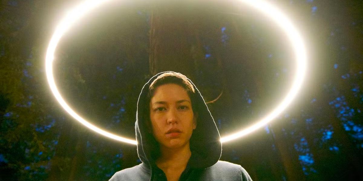 woman in a hoodie standing under trees and a circle of light