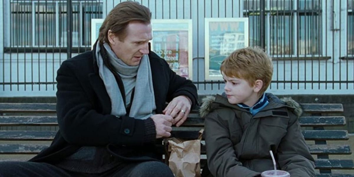 Liam Neeson as Daniel and Thomas Sangster as Sam talk on bench in Love Actually