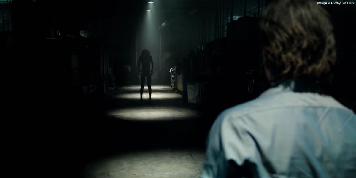 Frame from Lights Out with a man looking at a dark humanoid figure in a warehouse.