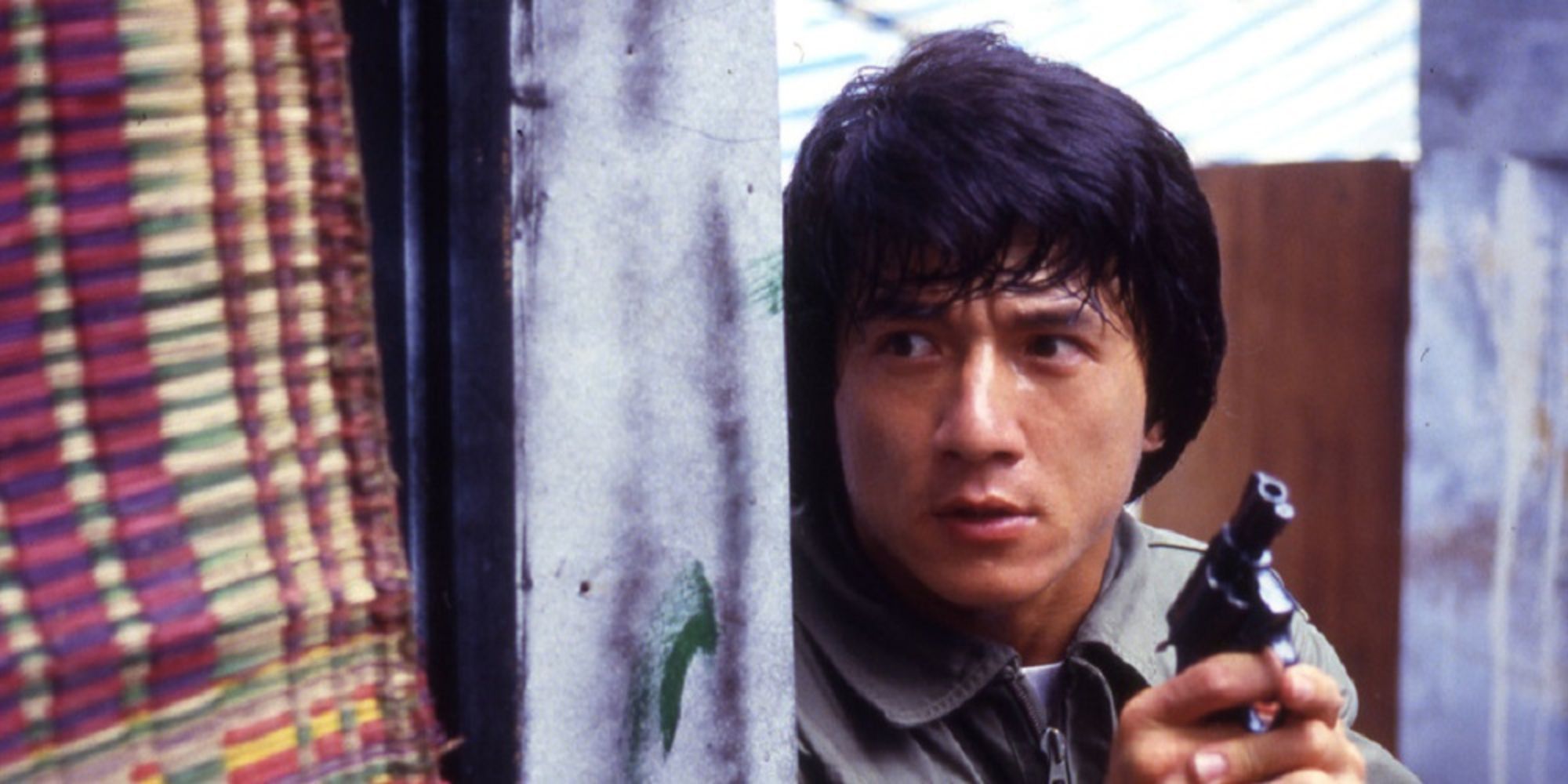 Jackie Chan holding a gun and looking from behind a wall in Police Story (1985)