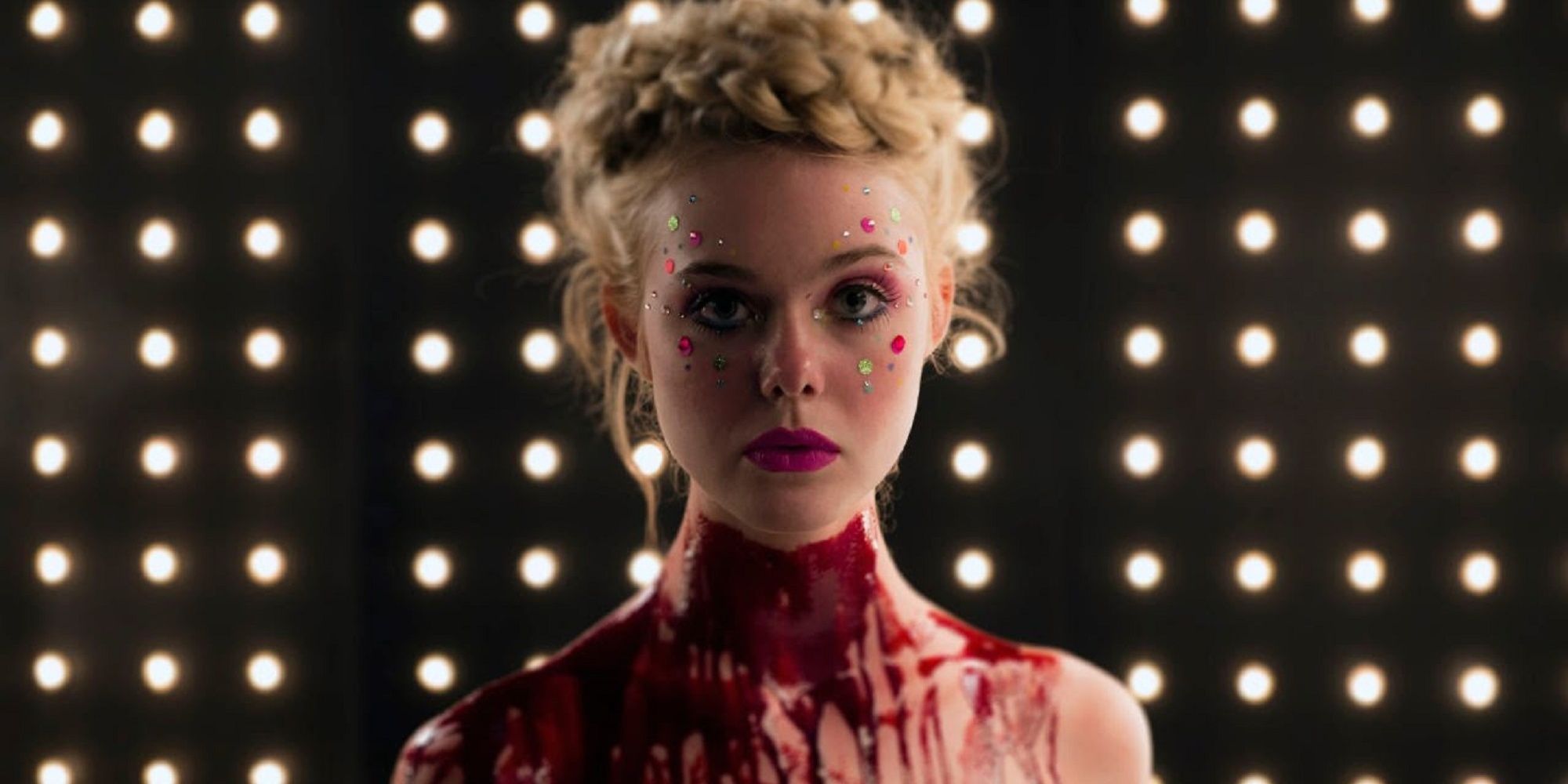 Elle fanning standing in front of a lit up background with blood around her neck in 'The Neon Demon.'