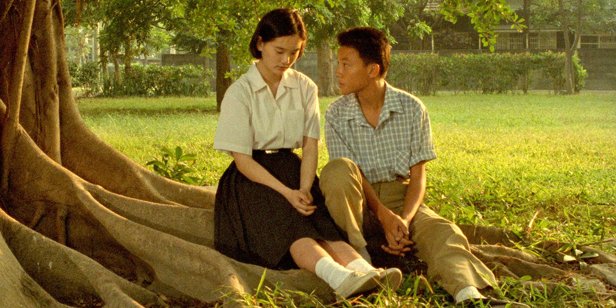 a teen boy and teen girl sitting under a tree