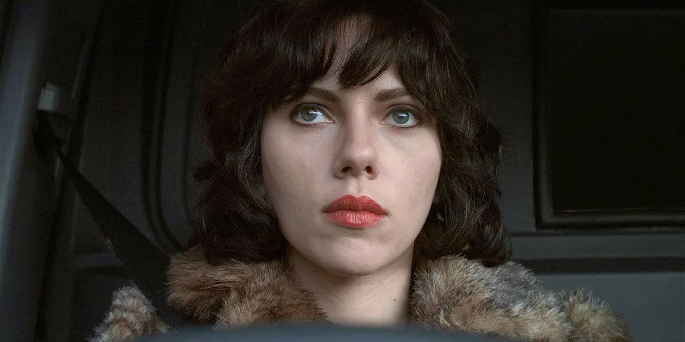 The Alien, played by Scarlett Johansson, sits in a car and looks at the distance in the film Under the Skin.