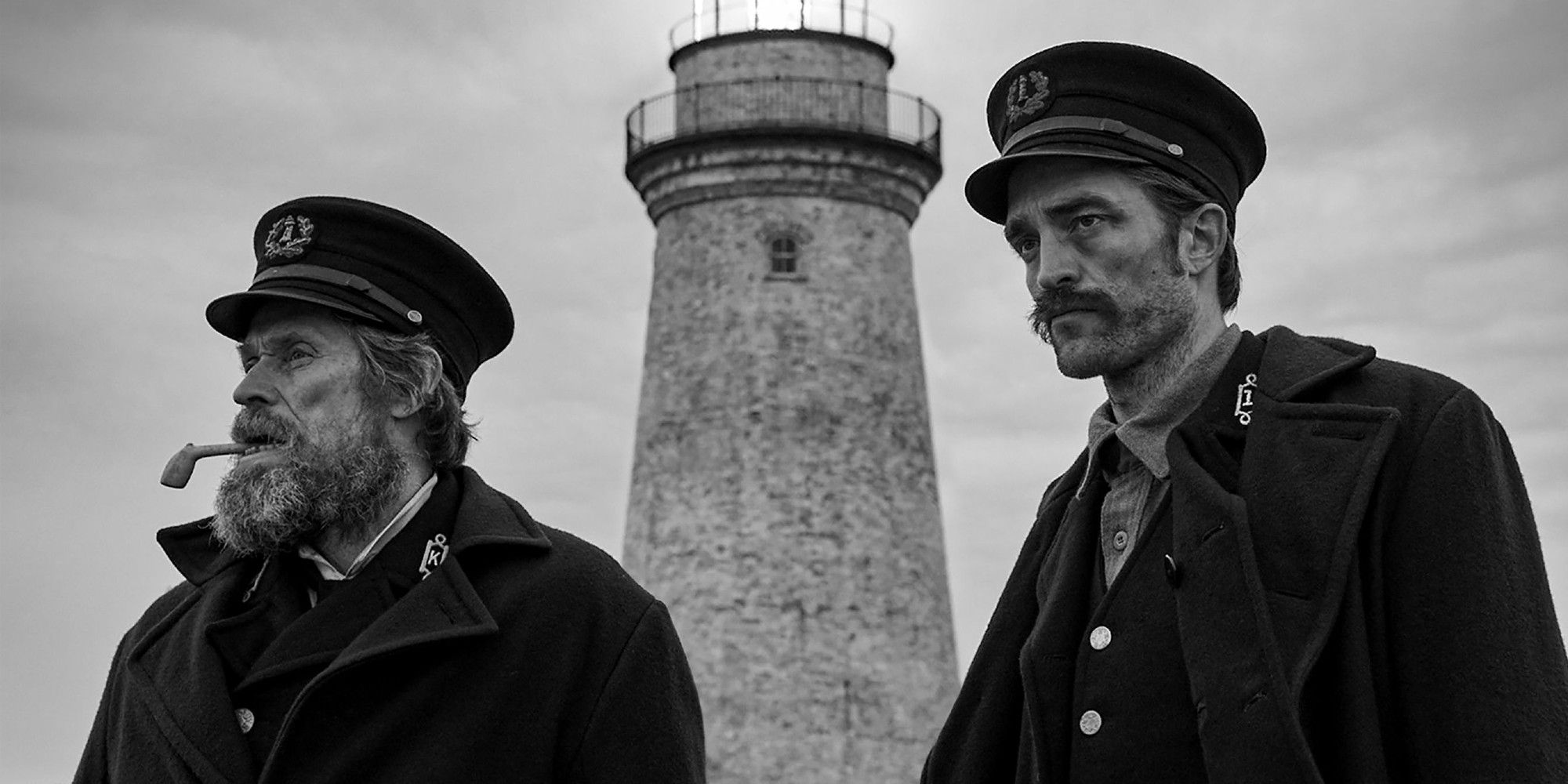 A medium black and white shot of Willem Dafoe and Robert Pattinson standing next to each other in 'The Lighthouse'