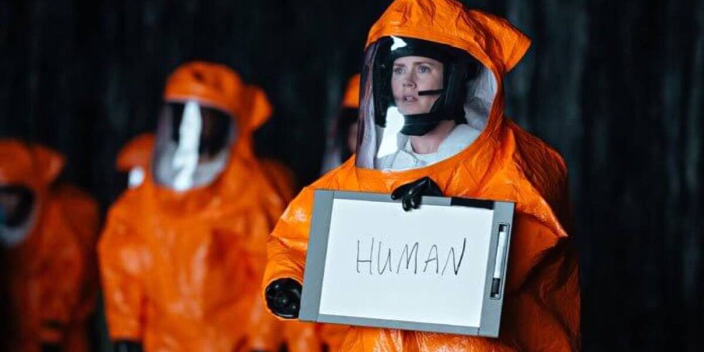 Louise Banks in a protective suit holding a whiteboard with the word "HUMAN" writen in Arrival.