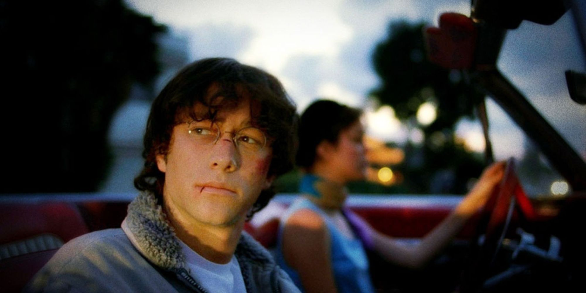 Joseph Gordon-Levitt in 'Brick' sitting in the passenger seat of a car, face bloody, looking off to the side.