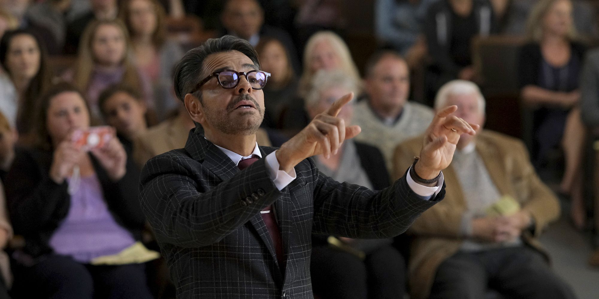 man with suit and glasses conducting an unseen group of musicians