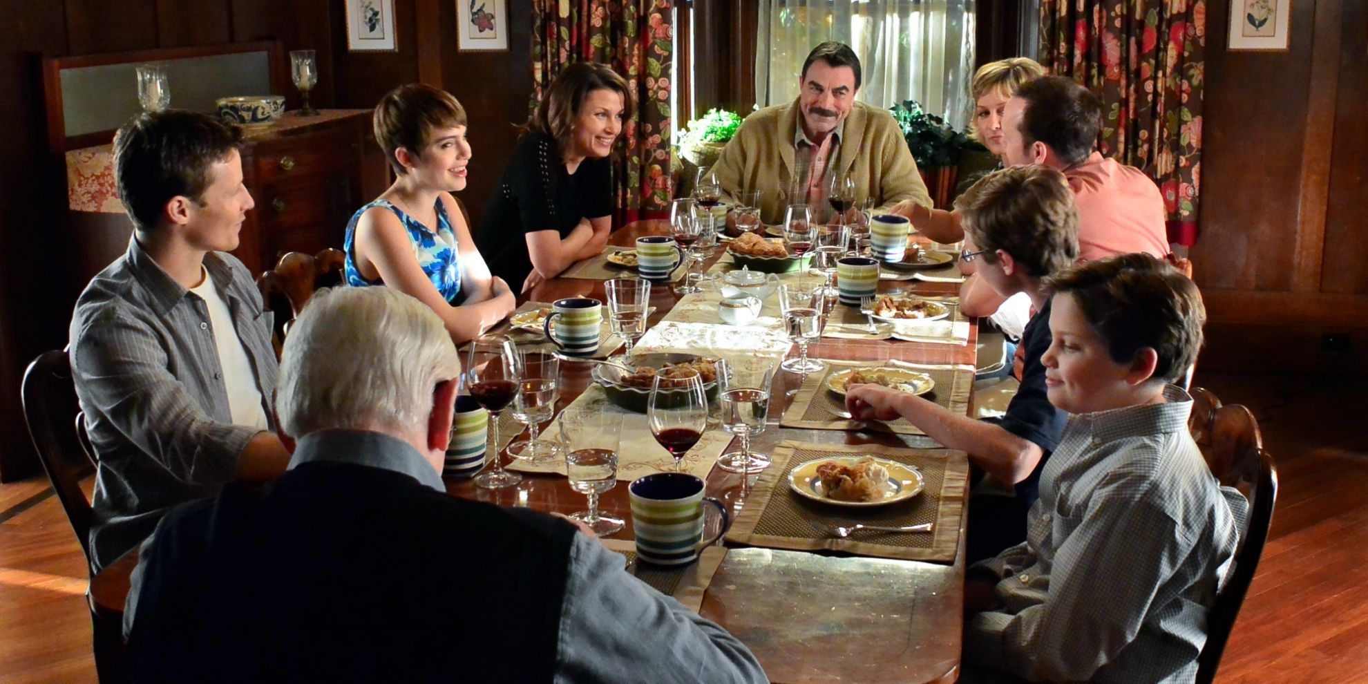 Tom Selleck as Frank Reagan, smiling and sitting with his family for Sunday dinner on Blue Bloods