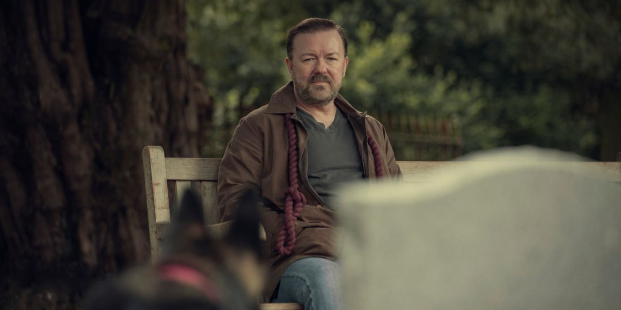 Ricky Gervais sitting on a bench looking sullen at a tombstone in After Life.