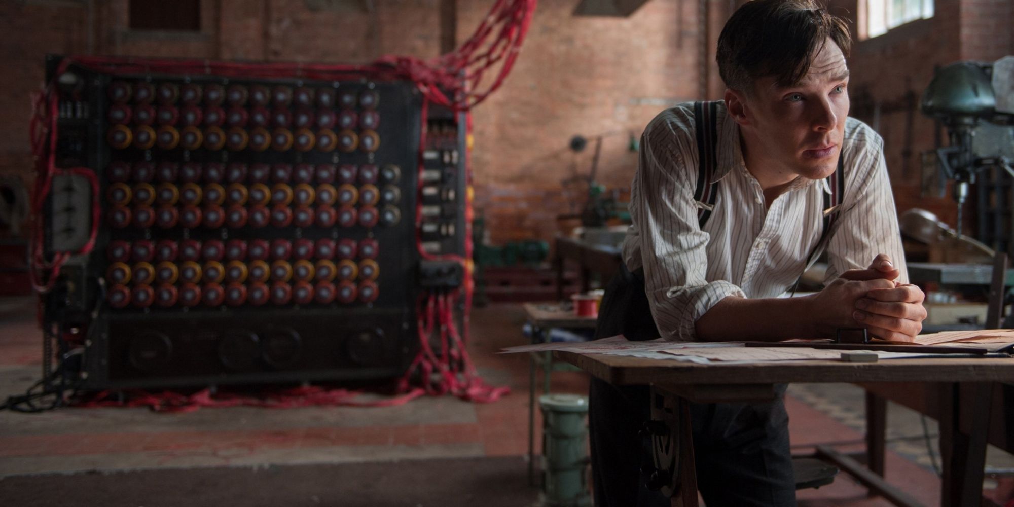 Benedict Cumberbatch as Alan Turing leaning on a table with his codebreaking machine in the background