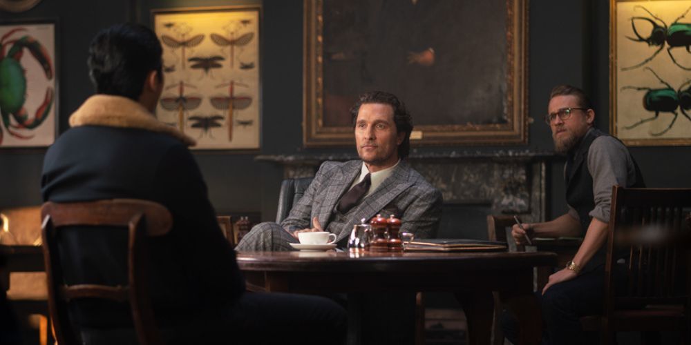 Matthew McConaughey senta-se à mesa e Charlie Hunnam senta-se atrás dele em The Gentleman